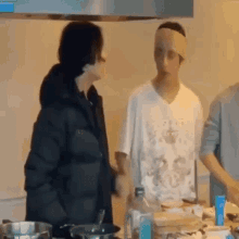 a man with a bandage on his head is cooking in a kitchen with other people .