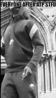 a black and white photo of a man in a hoodie and sweatpants smoking a cigarette .