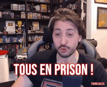 a man sitting in front of a microphone with the words " tous en prison " on the screen
