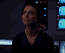 a woman in a scrub top is looking up in a dark room in front of a computer screen .