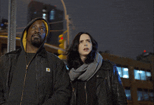 a man in a carhartt jacket stands next to a woman and a man in a daredevil suit