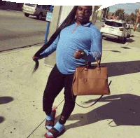 a man with long hair is standing on a sidewalk holding a purse .