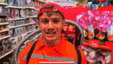 a man in an orange shirt and red hat is standing in a store with a vacuum cleaner .