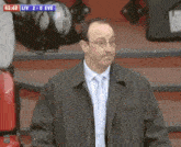 a man in a suit and tie is watching a soccer game with the score liv 2-0 eve
