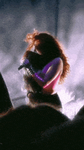 a woman in a pink top and purple gloves singing into a microphone