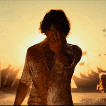 a man covering his face with his hand in front of a sunset with the name sanjo sebi below him