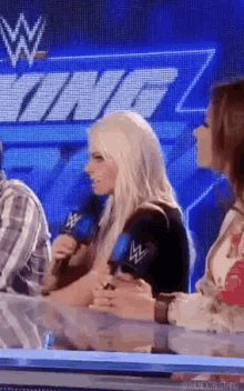 a woman is sitting at a table talking into a microphone while another woman watches .