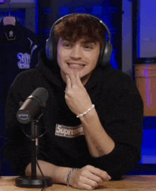 a young man wearing headphones and a black supreme sweatshirt is sitting in front of a microphone