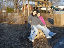 two girls are posing for a picture while sitting on a log