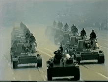 a row of military tanks are driving down a road