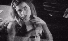 a black and white photo of a woman sitting at a table with her hair in a ponytail .
