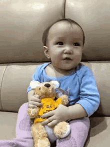 a baby is sitting on a couch holding a teddy bear in his hands .