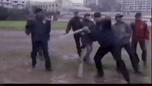a group of men are standing in a field fighting each other with a baseball bat .