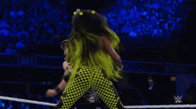 a wrestler in a green and yellow outfit is jumping over a referee