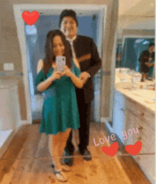 a woman in a green dress takes a selfie with a man in a black suit