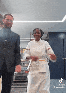 a man in a suit and a woman in a chef 's uniform are dancing in a kitchen with a tiktok hashtag