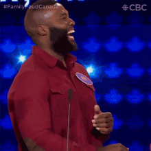 a man with a beard is laughing in front of a microphone while wearing a red shirt .