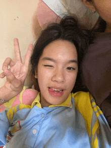 a girl laying on a bed with her eyes closed and giving a peace sign