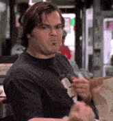 a man in a black t-shirt is eating a bag of chips