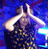 a person wearing a lemon print shirt holds their hands to their head