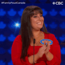 a woman in a red dress applauds in front of a microphone while wearing a name tag that says eliana