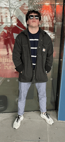 a man wearing sunglasses and a carhartt jacket stands in front of a mcdonald 's window