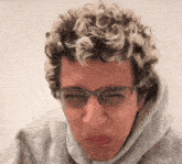 a man with curly hair wearing glasses and a grey hoodie
