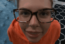 a woman wearing glasses and an orange sweatshirt looks at the camera