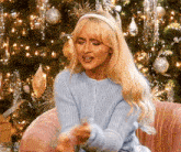 a woman is sitting in front of a christmas tree wearing a blue sweater and a headband .