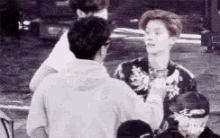 a black and white photo of a man talking to another man in a crowd .