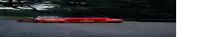 a red car is driving down a road next to trees .