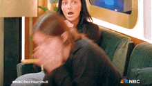 two women are sitting on a green couch with the nbc logo on the bottom