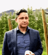 a man in a suit and blue shirt is standing in a field holding a bottle of beer .