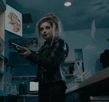 a woman in a black leather jacket is holding a gun in a dark room