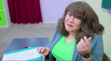 a woman wearing glasses and a green shirt is sitting at a desk in a classroom