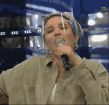 a woman singing into a microphone with a face shield on her head .