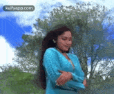 a woman in a blue sweater is dancing in front of trees and a blue sky .