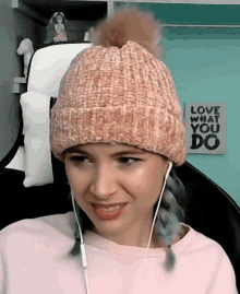 a woman wearing a pink beanie and ear buds with a sign that says love what you do behind her