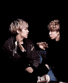 two young men are sitting next to each other in a dark room . one of the men is sitting on the other 's lap .