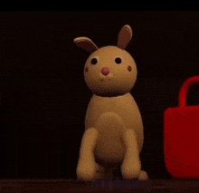 a toy rabbit is sitting on a table next to a red bag that says ' a ' on it