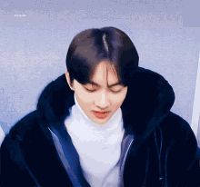 a young man wearing a black jacket and a white turtleneck sweater
