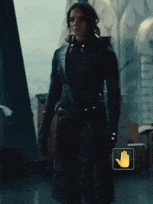 a woman in a black coat stands in front of a window with a yellow hand icon next to her
