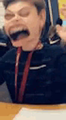a young boy is sitting at a table with his mouth open and making a funny face .