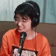 a girl wearing headphones and glasses is smiling in front of a microphone .