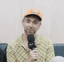 a man with a beard is holding a microphone while wearing an orange hat .