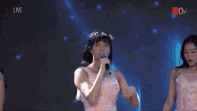 a girl in a pink dress singing into a microphone with the word live on the bottom