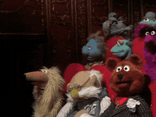 a group of stuffed animals are sitting in red chairs and one of them is wearing a suit