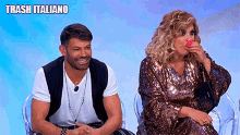 a man and a woman are sitting next to each other on a chair . the woman is eating a pink lollipop .