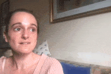a woman in a pink sweater is sitting on a couch in front of a picture on the wall .