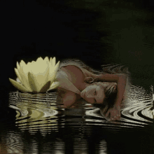 a woman is laying in a body of water next to a yellow flower